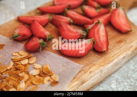 Geschnittene frische Erdbeeren und gebratene Mandelflocken zum Dekorieren und Dekorieren einer Baiser-Rolle Stockfoto