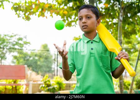 Seriuos Junge mit Cricket-Schläger und Ball warten darauf, in Haltung zu spielen - Konzept der selbstbewussten, seriöse Spiel spielen und Wochenende Urlaub Aktivitäten Stockfoto