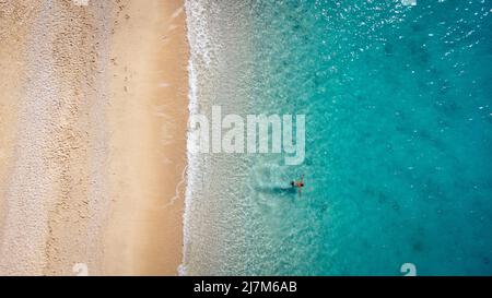 Luftaufnahme des Mannes, der im seichten Meerwasser schwimmt, den Strand und die sanfte türkisfarbene Meereswelle genießt. Tropisches Meer in der Sommersaison am Strand von Egremni Stockfoto