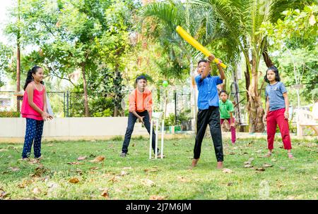 Kleines Kind, das beim Spielen von Cricket im Park auf den Ball trifft, um Punkte zu erzielen - im Gleichklang mit körperlichen Aktivitäten, Vitalität und Unterhaltung in der Kindheit