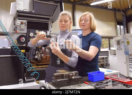 Eine junge Auszubildende erhält Unterricht von ihrem Trainer. Beide Frauen arbeiten als computergesteuerte numerische Steuerungstechniker. Sie werden gemeinsam auf ihrer Höhe gesehen Stockfoto