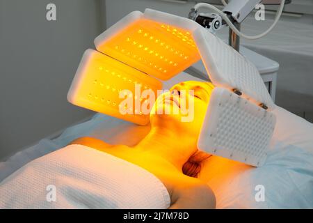 Eine ältere Frau durchläuft eine Gesichtsverjüngung. Frau Gesicht lt Rotlichtbehandlung in der Schönheitsklinik. Kosmetologie. Stockfoto