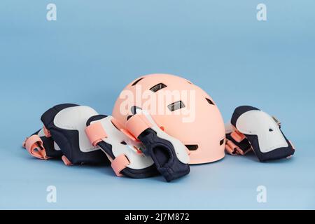 Draufsicht auf das Rollschuh-Schutzausrüstung-Set - Knie-, Ellbogen- und Handgelenkpolster sowie Helm in rosa Farben. Blauer Hintergrund flach lag Stockfoto