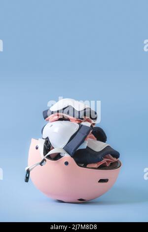Draufsicht auf das Rollschuh-Schutzausrüstung-Set - Knie-, Ellbogen- und Handgelenkpolster sowie Helm in rosa Farben. Blauer Hintergrund flach lag Stockfoto