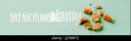 Einige Brotscheiben und Krümel auf grünem Hintergrund und der Text Breadcrumbing, in einem Panorama-Format als Webbanner oder Header zu verwenden Stockfoto