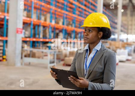 afroamerikanische junge Managerin, die Clipboard hält und während der Arbeit im Lager wegschaut Stockfoto