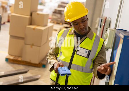 afroamerikanische junge männliche Lagerarbeiterin hält Stecker, der elektrische Ladegeräte betreibt Stockfoto