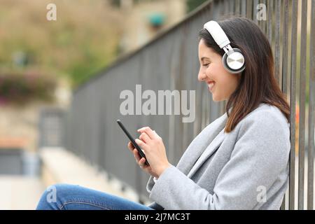 Seitenansicht Porträt einer glücklichen Frau, die auf dem Handy auf der Straße Musik hört Stockfoto