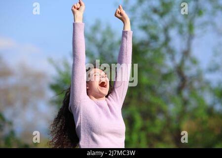 Eine aufgeregte Frau, die in einem Park die Arme hebt und einen guten Tag im Pullover feiert Stockfoto