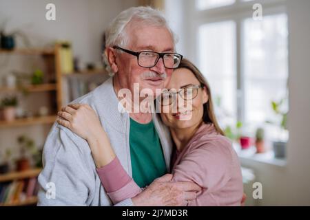 Die Erwachsene Tochter umarmte ihren älteren Vater, als sie ihn zu Hause besucht. Stockfoto