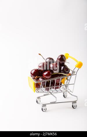 Kirsche in einem kleinen (kleinen) Lebensmittelkarren für einen Supermarkt. Spielzeugwagen mit Beeren auf weißem Hintergrund. Nahaufnahme, Kopierbereich, Banner. Stockfoto