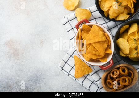 Snacks. Ungesunde Lebensmittel. Alle klassischen Kartoffelsnacks mit Erdnüssen, Popcorn- und Zwiebelringen und gesalzenen Brezeln in Schüsseln auf grauem Beton-Hintergrund Stockfoto