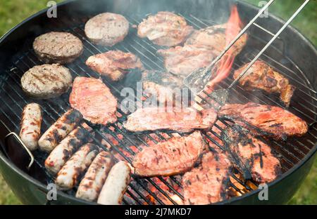 Barbecue-Kochen. Detail von Fleisch Kochen auf einem Holzkohlekessel Grill in einem Garten, Großbritannien Stockfoto