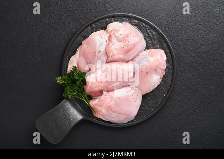 Rohes Hühnerschenkelfilet ohne Haut mit Kräutern und Gewürzen auf schwarzem Hintergrund. Geflügelfleisch auf dem Bauernhof. Draufsicht mit Kopierbereich. Modell. Stockfoto