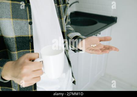 Pillen, steht ein junger Mann in der Küche und hält Pillen in der Hand, ein junger Erwachsener sieht Pillen in der Handfläche, Ratschläge des Arztes und Drogenkonsum Stockfoto