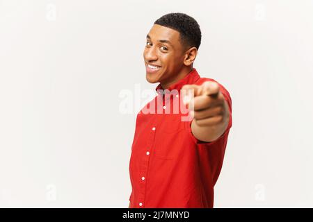 Fröhlicher afroamerikanischer Mann im roten Hemd zeigt Zeigefinger auf Kamera isoliert auf weißem Hintergrund, hübscher multirassischer Kerl, der dich auswählt und mit einem Lächeln anzeigt Stockfoto