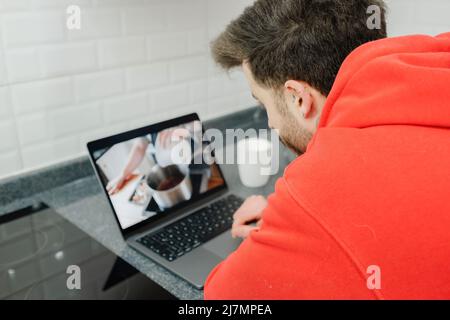 Junger Mann beim Kochen Video Rezept auf Laptop. Junger Mann in einem Lernen zu kochen, während ein Webinar auf einem Computer in der Küche zu Hause. Stockfoto