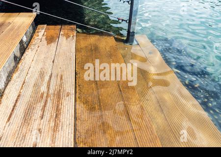 Nahaufnahme der natürlichen Holztreppen einer Lärchenleiter in das klare blaue Wasser des Sees, des Meeres oder des Teichs. Wasserdurchschlag aus Holzmaterial. Feuchtigkeitsbeständig Stockfoto