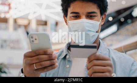 afroamerikanischer Mann Kunde in medizinischer Maske Eingabe von Bankkreditkartendaten in Handy-App zahlt Kauf Waren Online-Dienstleistungen Stockfoto