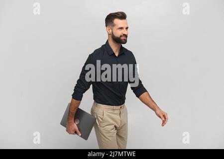 Hochformat von der Taille bis zum Lächeln des positiven Mannes, der den Laptop in den Händen hält und irgendwo hingeht. Innenaufnahme des Studios isoliert auf weißem Hintergrund Stockfoto