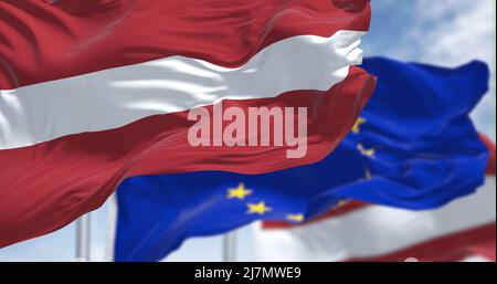 Detail der im Wind winkenden Nationalflagge Lettlands mit verschwommener flagge der europäischen Union im Hintergrund an einem klaren Tag. Demokratie und Politik. Eu Stockfoto