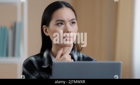 Thinking Student Mädchen asiatisch nachdenklich Frau Porträt sitzt vor dem Laptop Online-Aufgabe auf der Suche nach Problemlösung fühlt sich zweifelhaft tief in Stockfoto