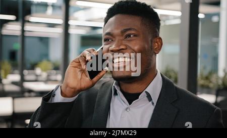 Afrikanischer Geschäftsanalyst Manager lächelnder Mann, der am Handy Kundenberatung spricht und in Innenräumen emotional Geschichten erzählt, die online gemacht werden Stockfoto