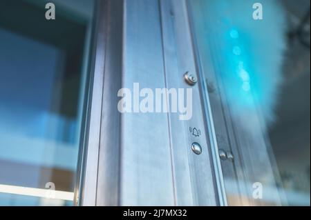 Detail einer modernen Metall- und Glastür mit einer Türklingel in einem Gebäude Stockfoto