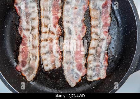 Knusprig rauchig gebratener Speck in Scheiben oder Streifen. Ungesunde fetthaltige Lebensmittel, fetthaltige Zutat. Rot dünne Scheibe oder Streifen oder Raschers Speck wird in einer Pfanne gebraten, Schweinefleisch Stockfoto