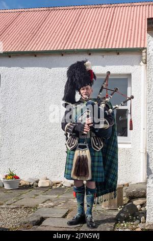 Männlicher Darsteller, der Dudelsack spielt, während er ein traditionelles schottisches Kostüm trägt: Blauer und grüner Tartan-Kilt und Accessoires, Kilberry, Schottland, Großbritannien Stockfoto