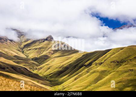 Sonnenlicht und Schatten auf den grasbedeckten Hängen der Drakensberg-Berge in Südafrika, während der Morgennebel wegzieht Stockfoto