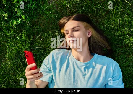 Junger Mann mit Smartphone in den Händen auf grün grasbewachsenem Hintergrund Stockfoto