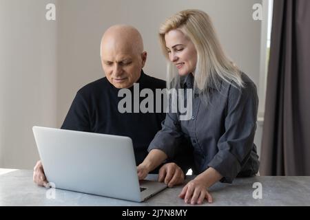 Frontansicht Happy Elderly 70s grauhaariger Mann lernt mit Hilfe von Computersoftware mit fürsorglicher erwachsener Tochter, älteren Menschen im Ruhestand und moderner Technologie Stockfoto