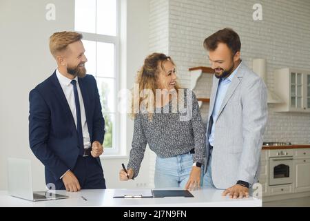 Ein glückliches Paar unterzeichnet während des Gesprächs mit dem makler im Haus einen Pacht- oder Kaufvertrag. Stockfoto