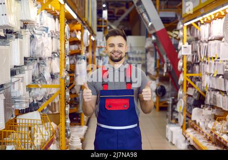 Ein glücklicher Verkäufer im DIY Store garantiert beste Qualität der Waren, lächelt und zeigt Daumen nach oben Stockfoto