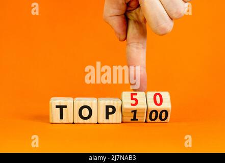 Von Top 100 bis 50 Symbol. Geschäftsmann dreht Holzwürfel und ändert die Begriffe Top 100 zu Top 50. Schöner orangefarbener Tisch und Hintergrund. Unternehmen Stockfoto