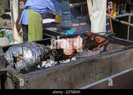 Blick auf den einfachen Holzkohlegrill mit Spieß-Braten auf dem deutschen Bauernmarkt Stockfoto