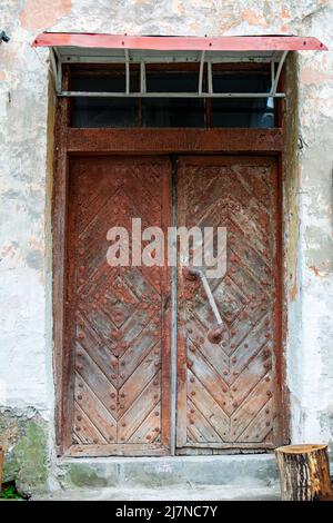 Eingangstür zu einem alten Mehrfamilienhaus mit abblätternden Wänden. Eine alte Tür mit rissiger Farbe und einem massiven abgenutzten Griff. Stockfoto