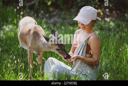 Einheit mit der Natur. Mädchen füttern bambi-Hirsche. Konzept der wilden Tiere. Frau, die das Rehkitz füttert. Tier im Park. Stockfoto