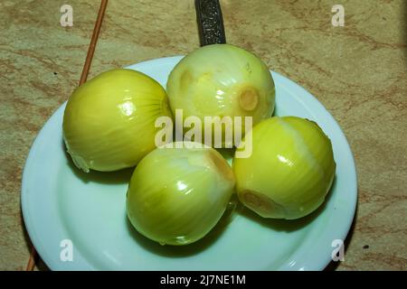 Geschälte Zwiebeln auf einem weißen Teller werden zum Schneiden vorbereitet. Stockfoto