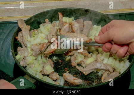 Schweinefleisch und gehackte weiße Zwiebel, in einer heißen Pfanne mit Öl gebraten, Nahaufnahme. Stockfoto