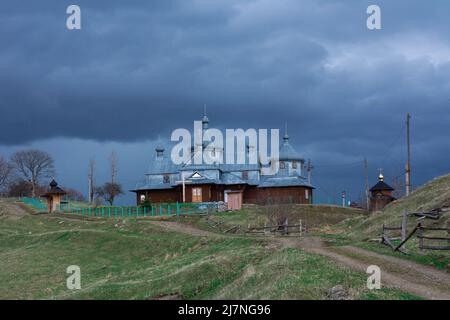 Kirche mit einem Metalldach und Kuppeln auf einem Hügel. Dramatischer Himmel mit Gewitterwolken über der Kirche. Ländliche Kirche in den ukrainischen Karpaten. Stockfoto