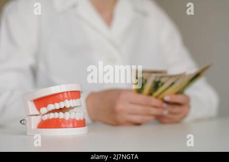 Zahnärztlicher künstlicher Kiefer. Frau Zahnärztin Zählen Geld auf dem Hintergrund. Teures Zahnpflegekonzept. Stockfoto