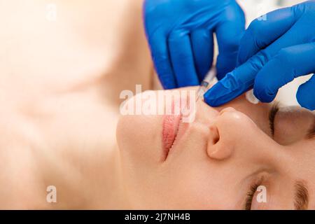 Nahaufnahme der Hände eines Kosmetologen, der Botox-Injektionen in die weiblichen Lippen macht. Korrektur der Lippenform, Lippenvergrößerung. Stockfoto