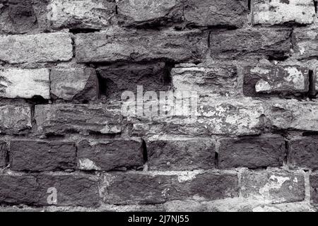 Alte Steinwand mit abblätterndem Putz. Rissige Mauerwerk, rissige Reste von Farbe und Zierleisten. Textur der alten Ziegelwand. Stockfoto