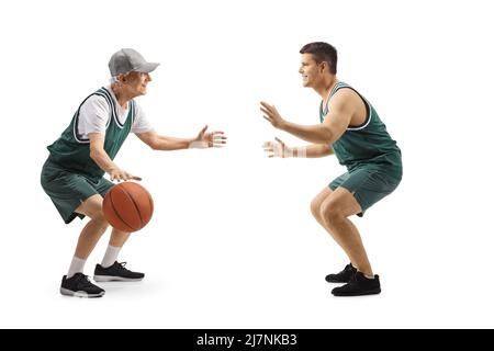 In voller Länge Profilaufnahme eines jungen und älteren Mannes in grünen Trikots, der auf weißem Hintergrund isoliert Basketball spielt Stockfoto