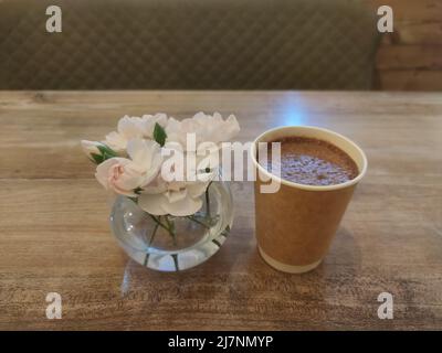 Kakao und Blumen in der transperenten Vase auf dem Holztisch. Morgenkaffee, Cappuccino, Latte und Gebäck. Blassrosa Rosen Stockfoto