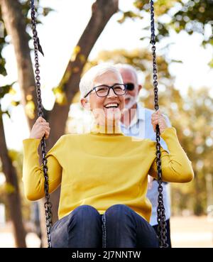 Seniorenpaar glücklich Schaukel Park Liebe aktiv gesund Lebensstil glücklich Spaß Freizeit Stockfoto