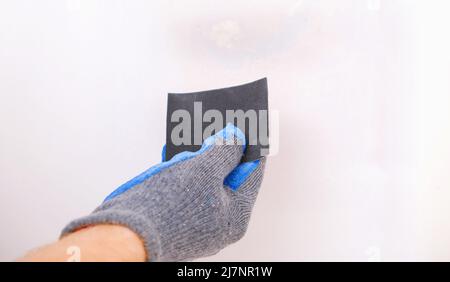 Ein Mann putzt alte Farbe an einer Holztür mit Schleifpapier. Glätten von Unregelmäßigkeiten. Stockfoto