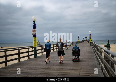 Besucher begeben sich an einem grauen Tag auf den Pier in Seal Beach. Die Pfosten auf dem städtischen Pier wurden in Blau und Gelb, den Farben von Ukra, dekoriert Stockfoto